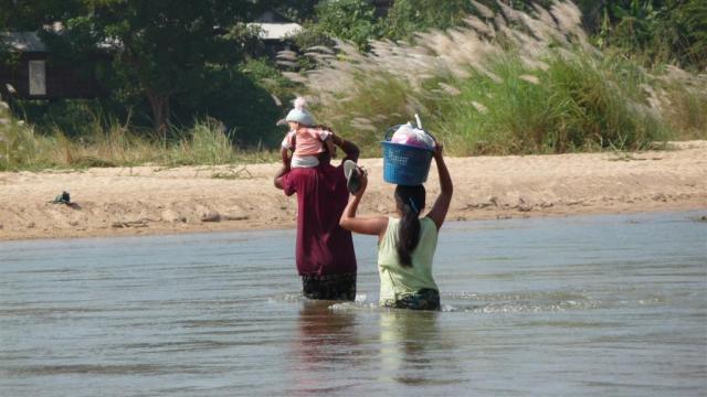 A man helps a woman and her baby cross back to the Burma side. 